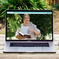 Ein Laptop steht auf einem Holztisch. Auf dem Bildschirm ist Doris Kirch zu sehen.