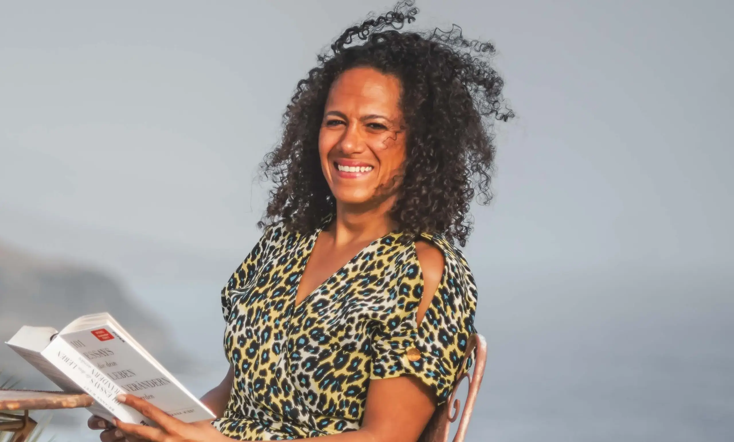 Foto von Ingrid Berger, die in die Kamera lächelt und ein aufgeschlagenes Buch in ihren Händen hält.