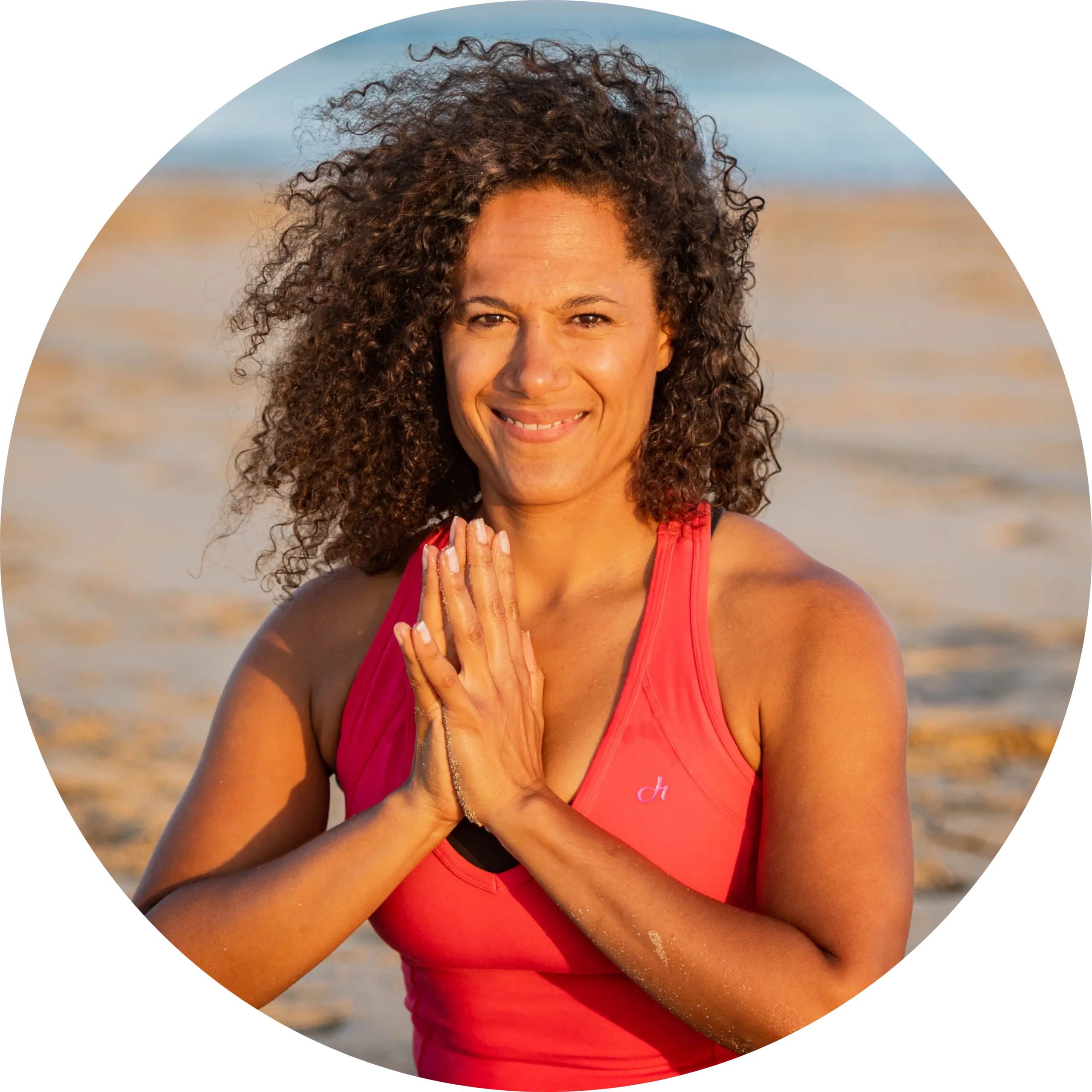 IngridBergerDFME Ingrid Berger sitzt im Sand, hat die Hände vor der Brust gefaltet und lächelt in die Kamera