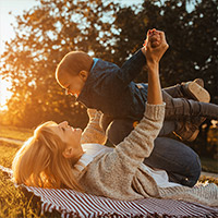 Frau spielt mit Kind auf einer Picknickdecke auf einer Wiese.