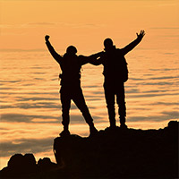 Zwei Menschen stehen auf einem Felsen im Sonnenuntergang.
