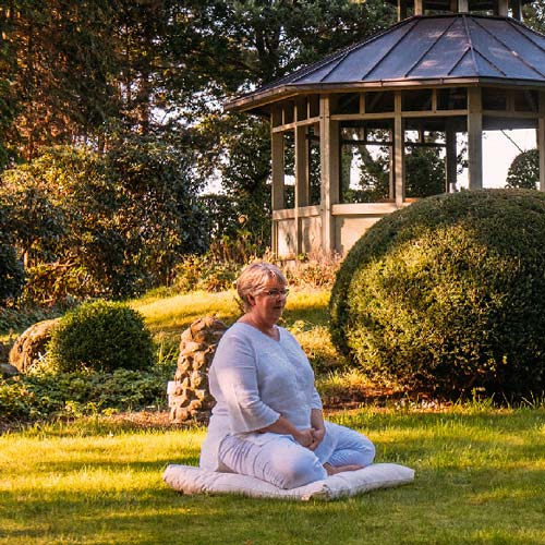 Doris Kirch sitzt auf einem Kissen auf einer Wiese und meditiert.