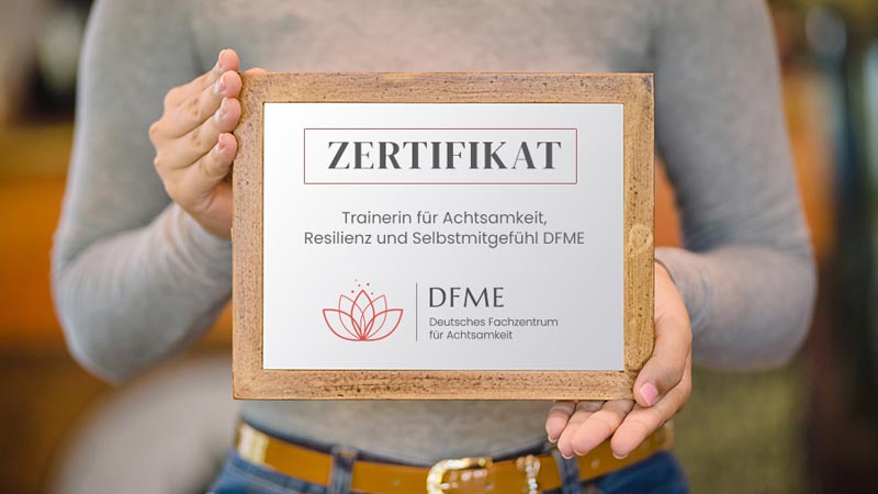 Frau hält das DFME Zertifikat als Trainerin für Achtsamkeit, Resilienz und Selbstmitgefühl in den Händen