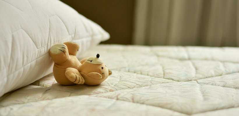 Kleiner Teddy, liegt entspannt auf dem Rücken auf dem Bett