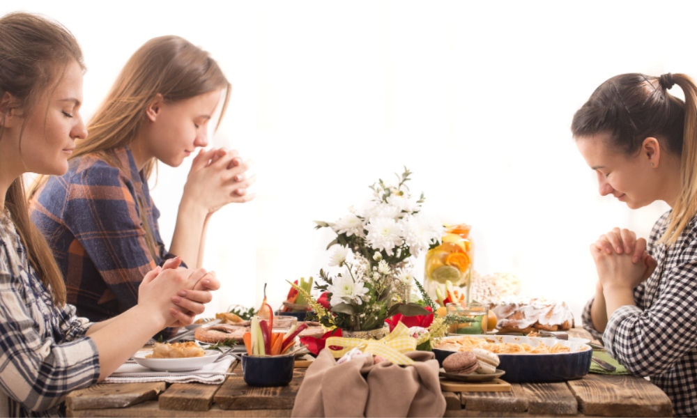Drei Frauen sitzen am gedeckten Tisch und beten bevor sie essen